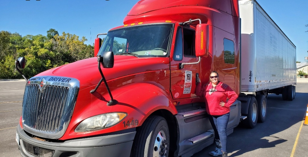 Woman in red jacket and jeans standing in front of red semi truck cab