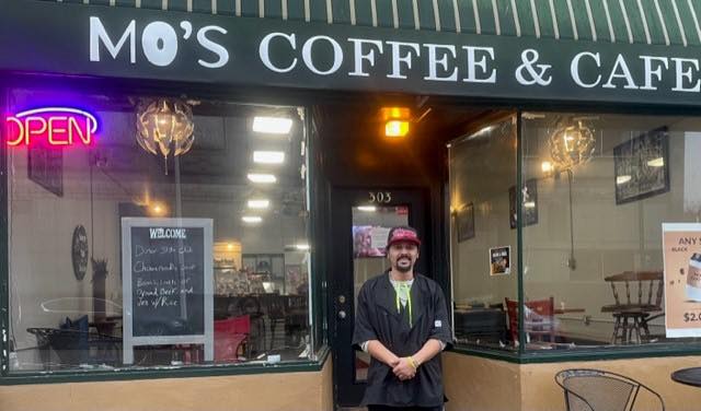 Man in a work uniform with cap standing in front of Mo's Coffee & Cafe