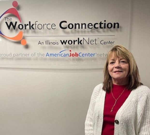 Photo of staff member Kelly introducing a story about how Kelly went above and beyond in helping a customer. Kelly is standing in front of a The Workforce Connection sign and has light hair, is wearing a red shirt with a white cardigan sweater.